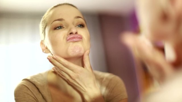 girl looks in the mirror, not pleased with the appearance, pulls the skin. Ugly, aging skin. Allergic to cosmetics, fear of aging, under eye circles, wrinkles. Low self-esteem, dysmorphic disorder. 