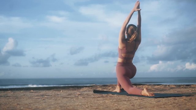 Woman does yoga exercises and stretches at morning on mat at beach, slow motion