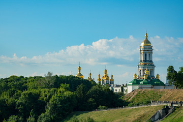 Fototapeta na wymiar Christian church on the green hills. The bell tower with golden domes. Christianity concept. Old church