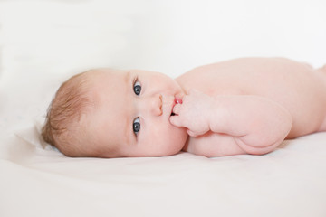 baby lies on a bed on a white background with a hand in his mouth. Teething. Four month old baby. A child nibbles his hand. Selective focus.