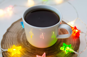 cozy still life with a cup of coffee on a wooden stand and colored garlands of stars