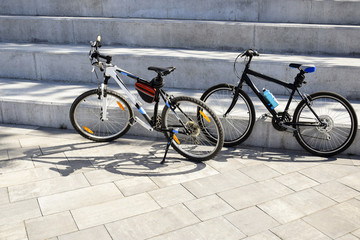 Fototapeta na wymiar Two bicycles are parked on large concrete steps. Shadows from bicycles fall on paving slabs.