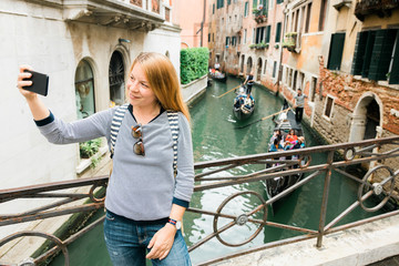 Fototapeta na wymiar Young female traveler taking a selfie by the canal in Venice, Italy
