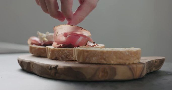 Slow motion man add pancetta to slice of ciabatta with fig marmalade