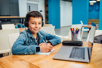 Child concentrated boy with laptop doing homework with headphone.