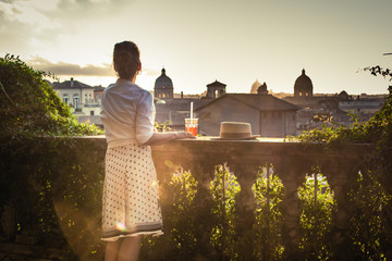 Young woman tourist fashion white dress with spritz cocktail in front of panoramic view of Rome...