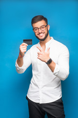 Portrait of a happy young businessman holding credit card and showing thumbs up isolated over blue background. Copy space. Successful man.
