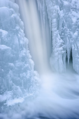Fototapeta na wymiar Winter landscape of the Comstock Creek cascade framed by ice and captured with motion blur, Michigan, USA
