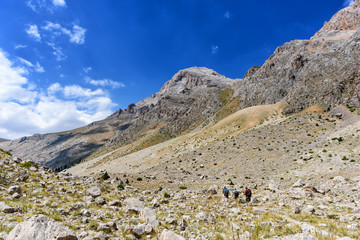 Turkey, Chamard - August 3, 2019: Tourists walk along the road through the mountain landscape in the Turkish national Park aladag in summer day, view from the back