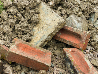 Close up of old bricks and a paving slab in a pile of earth on a building site