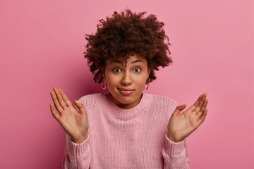 Clueless indecisive Afro American woman spreads palms, looks confused and unaware, cant find answer...