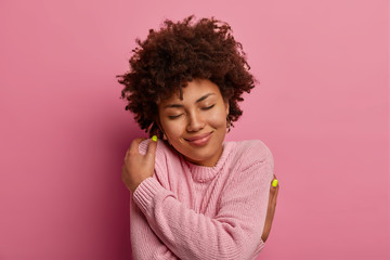 Self love and tenderness concept. Delighted gentle woman with curly hairstyle, embraces herself,...