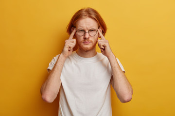 Distressed redhead man presses fingers to temples, has helpless face expression, suffers from...