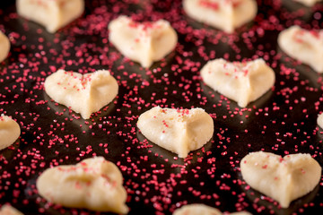 Heart shaped butter spritz cookies on baking sheet with red sugar sprinkles selective focus