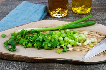 Close up of isolated sliced fresh spring onions (scallions) on wooden olive tree cutting board and japanese kitchen knife. Blue napkin, oil bottles and wood table background.