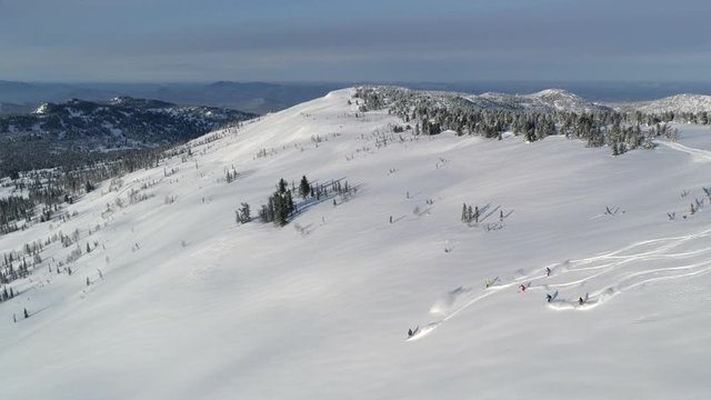 Aerial: Heli ski first track. Group of people skiing down the mountain valley. Epic free ride scene. Fresh powder. Skiing down the mountain with friends. Extreme freeride skiers skiing from the top