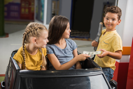 Kids Paying Money At Toy Petrol Station. Child Boy Taking Money And Looking At Camera. City Of Profession For Children.