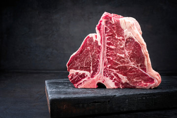 Raw dry aged wagyu porterhouse beef steak with large fillet piece as closeup on a black burnt...