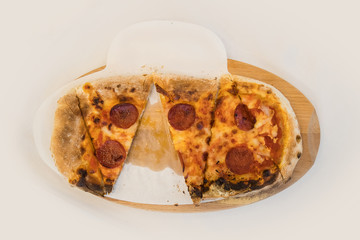 A small pizza cut in slices on a white background. Pizza with salami on a wooden plate on a white background. One slice is already missing, exposing greacy leftover.