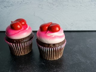 Two chocolate cupcakes decorated with white and pink frosting and red hearts on a black slate and gray shiplap background, perfect for love, Valentine’s Day, Mother’s Day or a birthday!