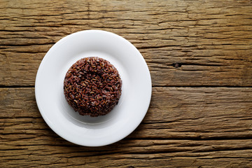 Cooked brown rice or riceberry rice on white plate on wood table