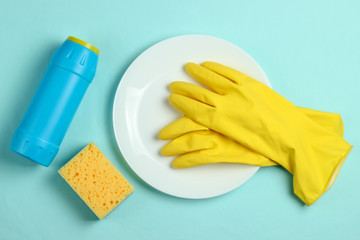 Washing dishes concept. Plate with a sponge and rubber gloves, bottle of detergent on a blue pastel background. Top view