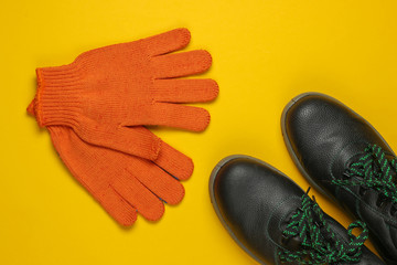 Leather work boots and gloves on yellow background. Worker safety. Top view