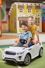 Happy kids playing together at entertainment center. Cute little boy and girl sitting in toy car in playroom.