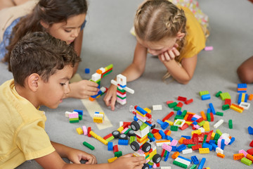 Kids playing block toys in playroom at nursery. Four children playing constructor while laying on...