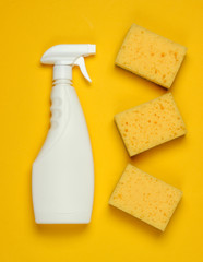 White bottle of spray for cleaning, sponges on yellow background. Top view. Minimalism