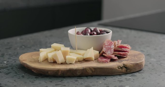 Slow motion man stick toothpicks in olives, cheese and fuet on olive wood board
