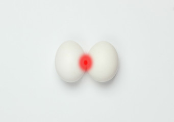 Prostatitis. Inflammation of the prostate. Allegorical photo of chicken eggs with red inflammation on white background. Top view