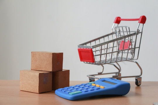 Calculator with Miniature shopping cart with parcel or paper cartons in trolley on laptop,E-commerce concept.