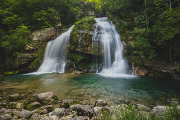 Long exposure of magical looking Virje waterfall in Slovenia, close to bovec. Dreamy and enchanting water falling down the cliff above the small alpine lake.