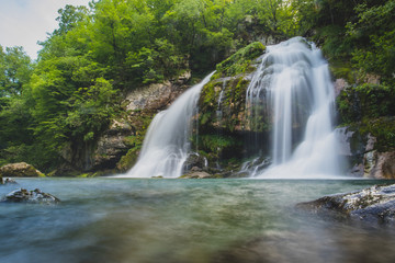 Fototapeta na wymiar Long exposure of magical looking Virje waterfall in Slovenia, close to bovec. Dreamy and enchanting water falling down the cliff above the small alpine lake.