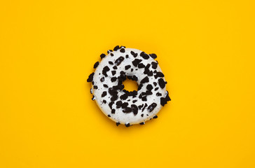 Glazed donut sprinkled with chocolate pieces on yellow background. Sweets cake, unhealthy food. Top view