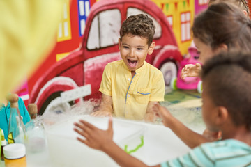 Emotional kid watching chemical experiment in playroom. Happy kids having fun in entertainment center. Birthday party celebration.