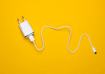 Charger with cable on yellow background. Top view
