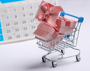 Miniature shopping cart and gift boxes with desktop calendar on white background. Holiday shopping, black friday, monthly special offer concept