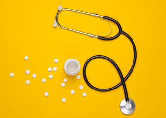 Medicine still life. Stethoscope with bottle of pills on yellow background. Top view.