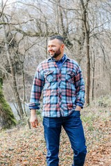 Bearded hipster man with serious face is thinking about something while standing outdoors against autumn fall with copy space, stylish brutal male with trendy look walking in park at sunset.