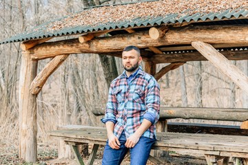 Bearded hipster man with serious face is thinking about something while standing outdoors against autumn fall with copy space, stylish brutal male with trendy look walking in park at sunset.