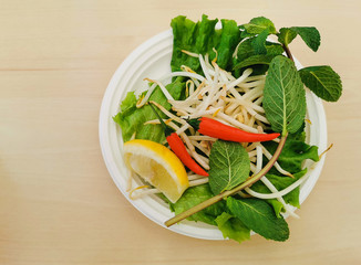 A typical garnish plate with every vietnamese beef pho soup with bean sprouts, chili pepper, lemon or lime wedges and aromatic herbs.