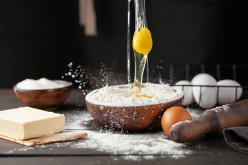 The raw egg is poured into a bowl of flour. Chef hands pouring flour powder on raw dough using...