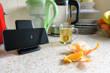 smartphone wireless charging on charging stand with 100 percent icon on screen on kitchen tabletop...