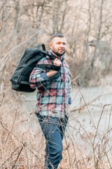 A young bearded guy with a backpack in the hat, traveller, hipster standing in the woods.