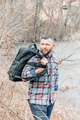 A young bearded guy with a backpack in the hat, traveller, hipster standing in the woods.