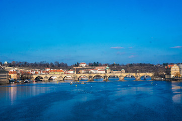 View of the Carles Bridge in Prague, Czech republic as seen from the Legion bridge overlooking Vltava river. Bright and bold blue colours of the water with birds in daylight.