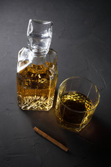 a rum in a decanter and a glass nearby lies a cigar on a dark background