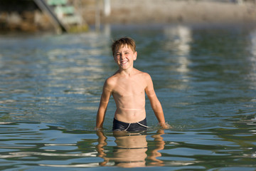 Jolly, little child stands in water of lake. Sunset lights. Positive expression.